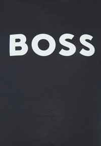 Juoda medvilninė marškinėliai su didelėmis balto bloko raidėmis priekyje, kuriose parašyta „BOSS“. Lygus paviršius su apvalia iškirpte.