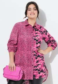 Hemd mit einem gespaltenen Design aus pinkfarbener Leopard- und Camouflage-Musterung. Der Stoff ist glatt, und das Hemd verfügt über Knopfverschlüsse und aufgerollte Ärmel.