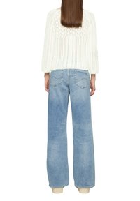 Weißer gestrickter Pullover mit strukturiertem Rücken, kombiniert mit hellblauen weiteren Jeans mit lässigem, gefranstem Saum und Gesäßtaschen.