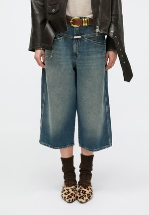 Blå viddebenede denimculotter med falmet finish, kombineret med brune ribstrikkede sokker og leopardmønstrede sko. Stylet med brunt bælte og læderjakke.