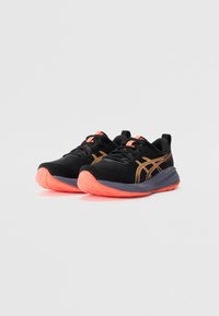 Black athletic shoes with a textured upper, orange accents, and a pink sole. Features a rounded toe and a cushioned midsole.