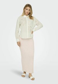 Cămașă albă ușoară cu un design floral perforat, asociată cu o fustă maxi roz moale din material răsucit și sandale albe. Detalii simple cu guler și nasturi.