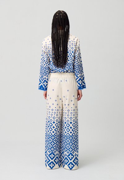 Mono de manga larga en color crema con patrones geométricos azules, que presenta una cintura elástica y corte de pierna ancha, con una textura suave y ligera.