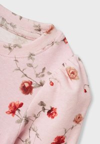 Rožinė gėlių ilgomis rankovėmis palaidinė su raudonais ir žaliais rožių raštais, tekstūruota medžiaga ir suglebusių pūstų rankovių detalės.