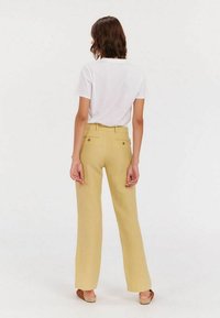 Pantalons large jaune clair avec deux poches arrière, assortis à un t-shirt blanc à manches courtes. Tissu lisse avec une coupe droite.