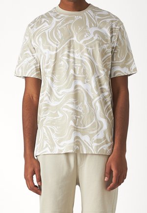 Mann trägt ein kurzärmeliges T-Shirt mit abstraktem Wirbelmuster in Beige und Weiß sowie dem "BOSS"-Logo, kombiniert mit hellbeigen Shorts.