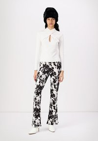 White long-sleeve top with a keyhole detail pairs with black and white cow-print flared pants; model wears a black fur hat and white heeled boots.