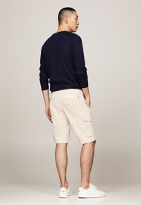Chemise à manches longues bleue marine, shorts cargo beiges et baskets blanches. Les shorts sont dotés de poches latérales et d'une coupe légèrement ample. Design épuré.