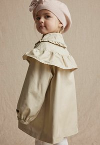 Beige jasje met een gerimpelde kraag, lange mouwen en elastische manchetten. Gecombineerd met een zacht roze gebreide baret. Gladde textuur, eenvoudig ontwerp.