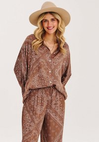 Hnědý outfit ve stylu paisley, tvořený dvěma kusy z hladkého materiálu, obsahující košili s knoflíky a volnými rukávy a kalhoty s elastickým pasem.