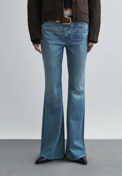 Jeans a zampa di un azzurro chiaro con finitura slavata, caratterizzati da un classico design a cinque tasche e una cintura marrone. La texture è in denim liscio.
