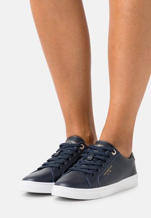 Marineblaue Ledersneaker mit weißen Gummisohlen, runden Schnürsenkeln, goldenen Akzenten und Markenlogo an der Seite. Glatte Textur.