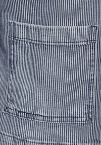 Tejido a rayas azul y blanco con un único bolsillo parches. La textura es suave, con costuras rectas a lo largo de los bordes y las costuras.