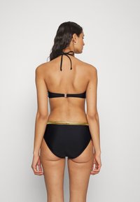 Juodas bikinis su kaklo šoneliu ir metaliniu auksiniu akcentu ant juosmens. Lygus paviršius, minimalistinis dizainas. Rodytas iš nugaros.