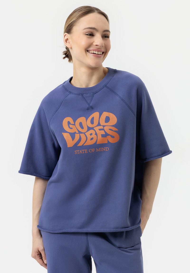 Paarse korte mouwen sweatshirt van textuurstof met een grote oranje print aan de voorkant waarop staat "GOOD VIBES STATE OF MIND".