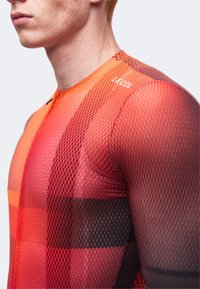 Gros plan d’une personne portant un maillot de cyclisme en mesh rouge et orange avec le texte « LE COL » sur l’épaule.