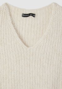 Maglione crema a scollo a V realizzato in tessuto a maglia testurizzato con una sensazione morbida. Etichetta visibile con nome del marchio e dettagli sulle taglie.