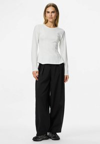 Bijela majica dugih rukava s okruglim izrezom, koja ima prilagođeno tijelo i raširene bokove, u kombinaciji s crnim širokim hlačama i crnim tenisicama.