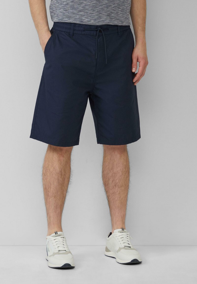 Marineblauwe shorts van een gestructureerde stof, met een elastische tailleband en trekkoord, en zijzakken, gecombineerd met witte sneakers.