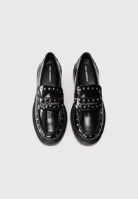 Mocassins en cuir verni noir avec des brides cloutées et une semelle épaisse. Présente des accents métalliques et une texture lisse et brillante.