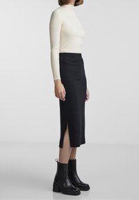 Pull à col roulé en maille côtelée crème, jupe midi noire en maille côtelée avec fentes, associée à des bottines à talons épais noires. Texture lisse, design ajusté.