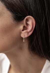 Pendientes dorados con tres cristales transparentes en un diseño lineal, con acentos en forma de diamante y redondos, que cuelgan por debajo del lóbulo de la oreja.