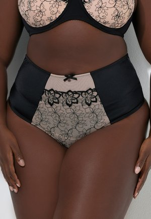 Mujer curvilínea vistiendo un conjunto de lencería de encaje floral en negro y beige de cintura alta, con un pequeño lazo en la pretina de la ropa interior.