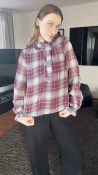 Chemise à manches longues à boutons, à carreaux bordeaux et blancs. Elle présente un col à volants et une coupe ample, associée à un pantalon noir.