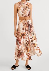 Robe maxi à col halter, motif floral dans des nuances de pêche et de marron, taille cintrée avec une ceinture beige et une fente sur le côté.