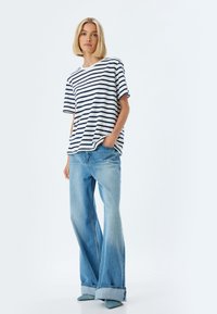 Stribet skjorte i hvid og marineblå, med korte ærmer, parret med lyseblå vidde jeans og teal spidse sko. Enkel design.