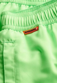 Shorts con cintura elastica verde realizzati in tessuto liscio, con un piccolo etichetta arancione con il logo "SUPERDRY". Design minimalista e senza motivi.