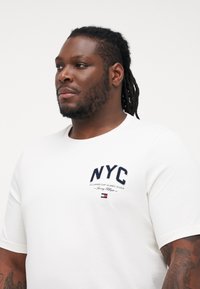Biely bavlnený tričko s krátkymi rukávmi a okrúhlym výstrihom, s námorníckym logom "NYC" a vyšitým textom nad malým akcentom loga.