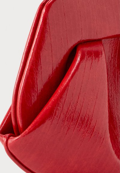Κοντινό πλάνο λαμπερής κόκκινης δερμάτινης τσάντας με ομαλές πτυχώσεις και ορατές ραφές.