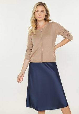 Beige ribbkardigan med knapper, parret med en marineblå satinskirt, der har en flydende silhuet og glat tekstur.
