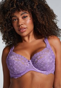 Lila spetsbehå med blommönster, underwire-stöd och justerbara band. Dekorativ rosett framtill. Mjuk, texturerad tyg.