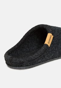 Black felt slipper with a rounded opening, textured surface, and a tan leather tag featuring the brand name. Simple, minimalistic design.