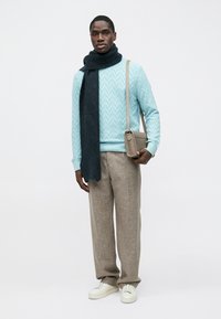 Pull texturé bleu clair, écharpe foncée, pantalon beige et baskets blanches. Comprend un petit sac à bandoulière gris.