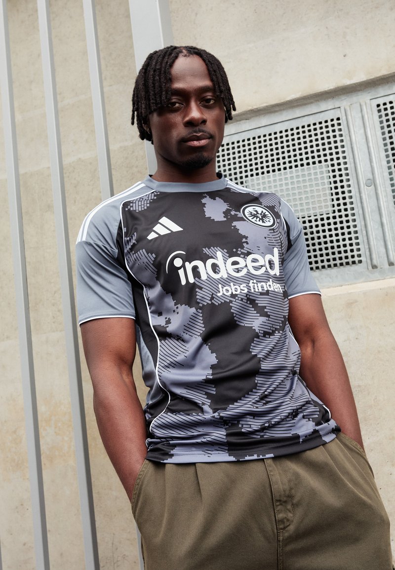 Camiseta de fútbol gris con estampado y mangas cortas, que presenta el logotipo de "indeed" en blanco y el logo de Adidas en los hombros.