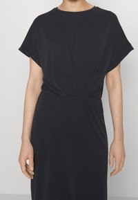 Schwarzes Kleid aus weichem, leichtem Stoff. Mit kurzen, umgeschlagenen Ärmeln und einem gerafften Bund bietet es eine lockere Passform. Sanfte Textur.
