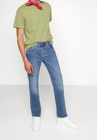 Camiseta de algodón verde, jeans de mezclilla azules y zapatillas blancas. Tejido ligero, corte recto, con un pañuelo rosa alrededor del cuello.