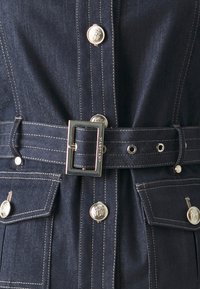 Mørkeblå denimkjole med sølvfarget detaljer, innsnurt midje med spenne, to frontlommer, og kontraststing.