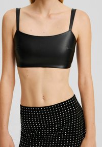 Svart fusk läder kort top med fyrkantig halsringning och tunna axelremmar, kombinerat med en svart kjol med metallisk nitar.