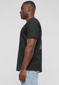 Sort kortærmet t-shirt med rund hals, prydet med farverigt grafisk print på ryggen, sammen med lyseblå denim jeans.