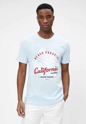 Jasnoniebieska koszulka z krótkim rękawem z graficznym nadrukiem przedstawiającym palmy oraz tekstem „Beach Paradise California surfing west coast” w kolorze czerwonym i niebieskim.
