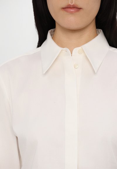 White button-up shirt with a classic collar, made of smooth fabric. Features small buttons and a clean, streamlined design.