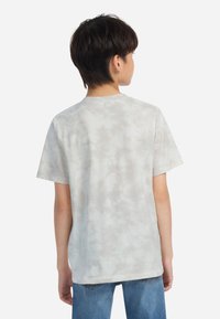 Gaišpelēka tašīte ar krāsainām svītrām, īsām piedurknēm, brīva piegriezuma un apaļu kakla izgriezumu; kombinēta ar ziliem džinsiem.