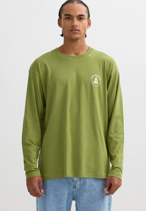 Camiseta de manga larga de color verde musgo hecha de algodón. Presenta un logo circular blanco en el área del pecho izquierdo. Corte relajado y cuello redondo.
