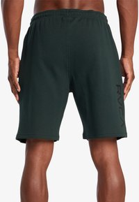 Shorts d'entraînement vert foncé en mélange de coton, avec une taille élastique et un logo imprimé noir sur le côté gauche.