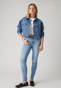 Chaqueta de mezclilla en azul claro con un diseño recortado, mangas largas, cierre de botones y dos bolsillos en el pecho, combinada con jeans ajustados de mezclilla azul claro.