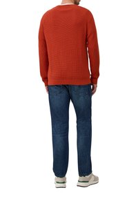 Roter gestrickter Pullover mit gerippter Textur, Rundhalsausschnitt und langen Ärmeln, kombiniert mit blauen Jeans und grauen Sneakern. Sichtbare Nähte und designdetails.